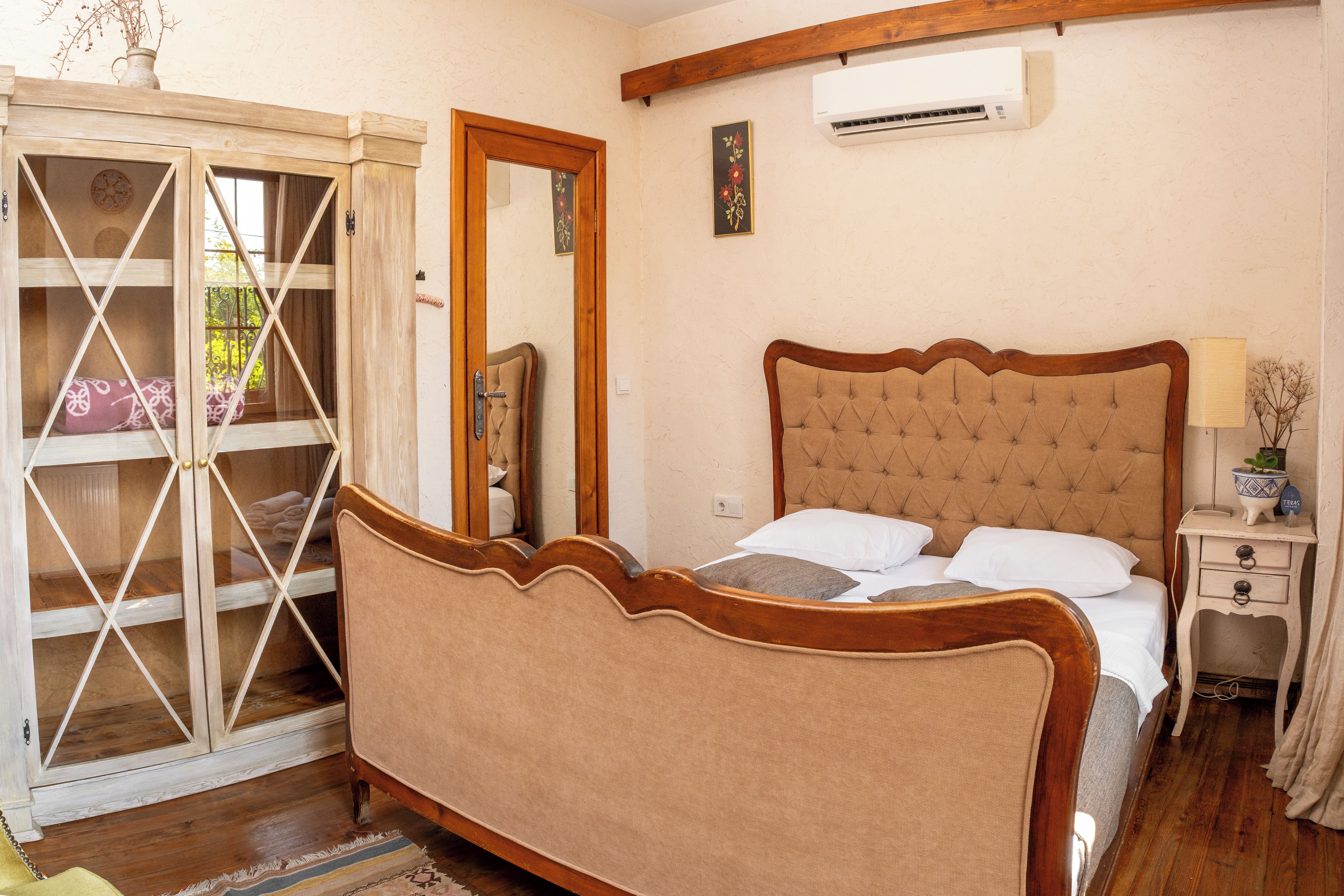 A bedroom with a wooden bed, a nightstand, an air conditioning unit, and a sliding glass door leading to a balcony.