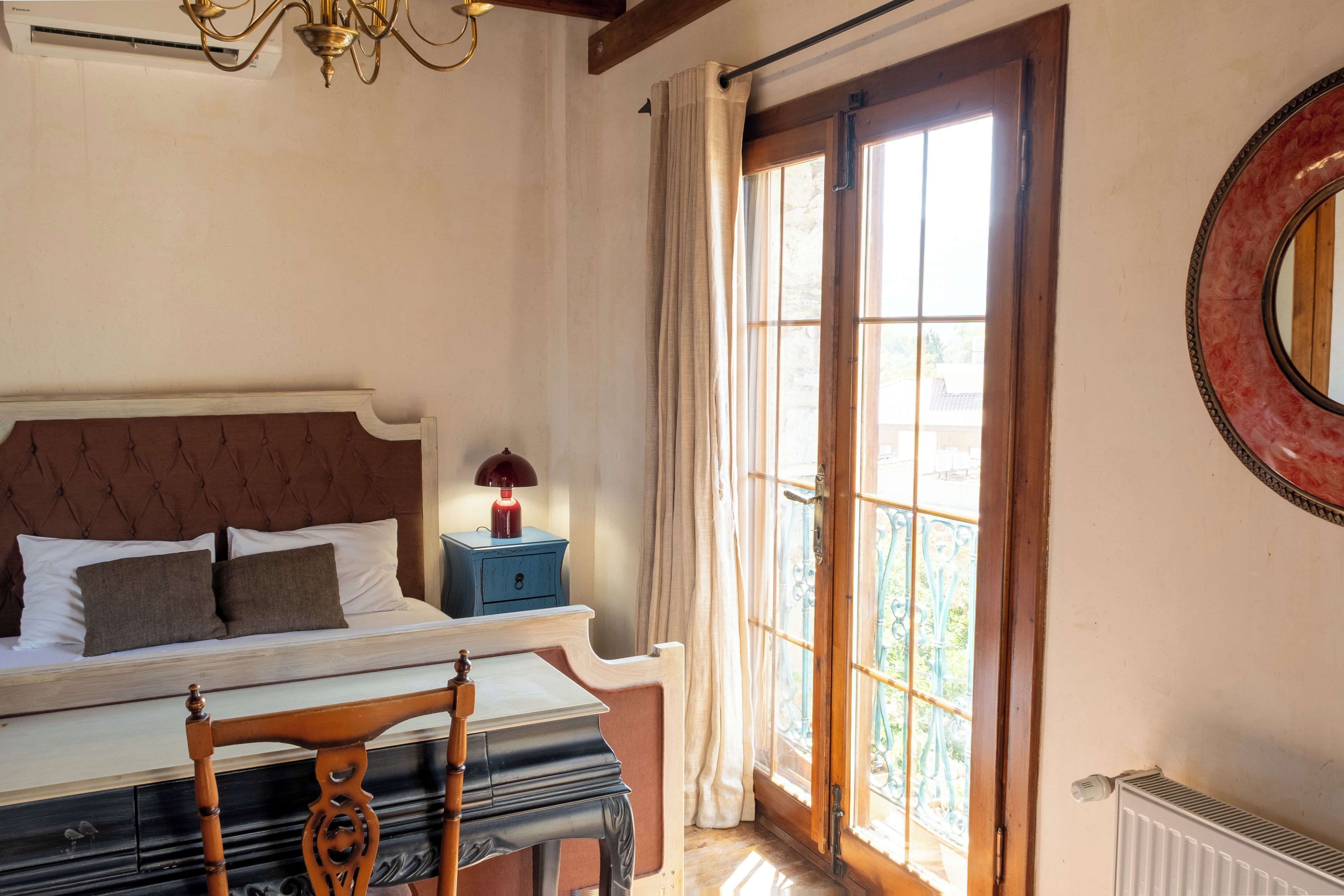 A bedroom with a bed, bedside table, lamp, and a view of the outdoors through a window.
