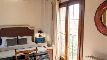 A bedroom with a bed, bedside table, lamp, and a view of the outdoors through a window.