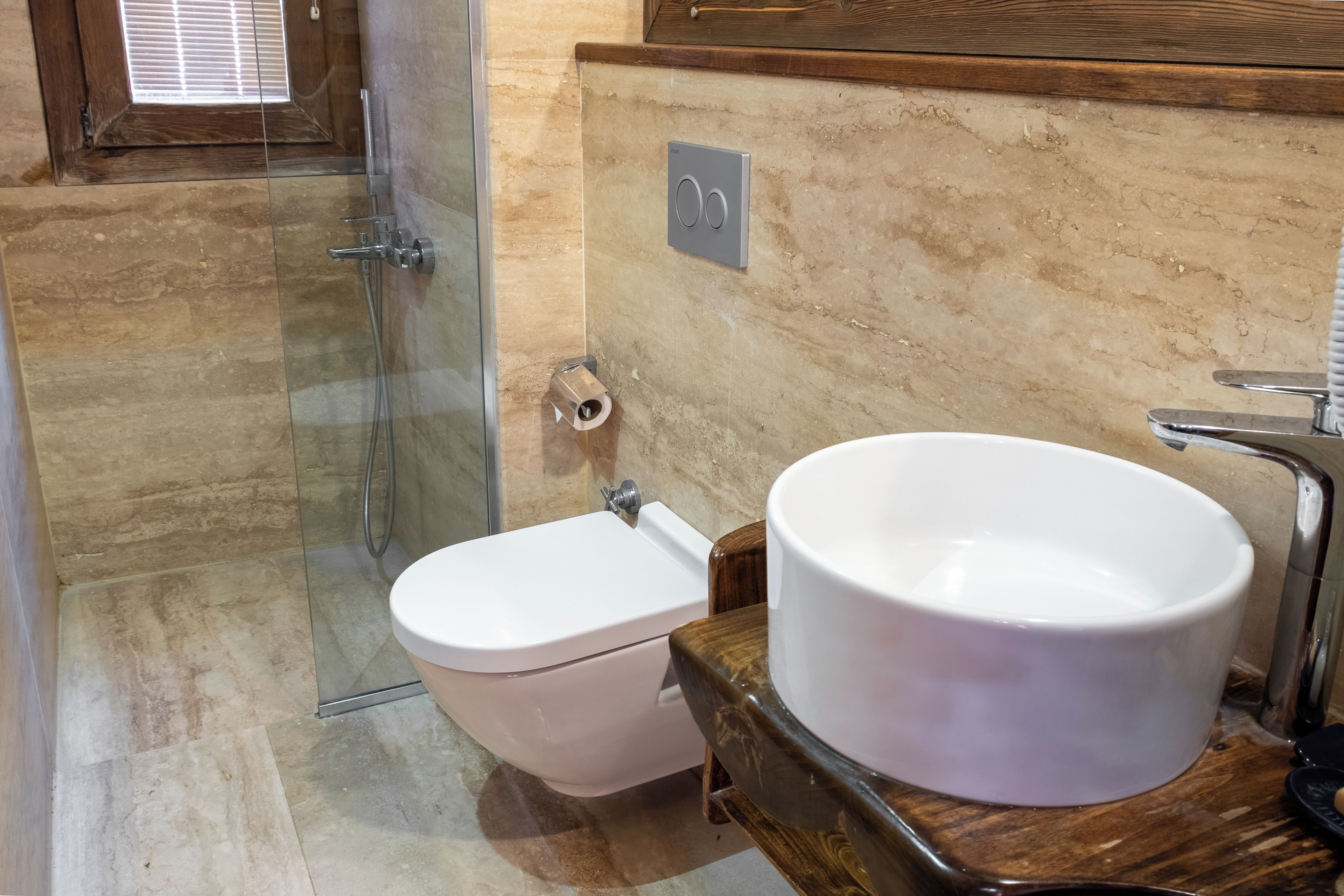 A bathroom with a glass shower enclosure, a white toilet, and a large white basin on a wooden countertop.