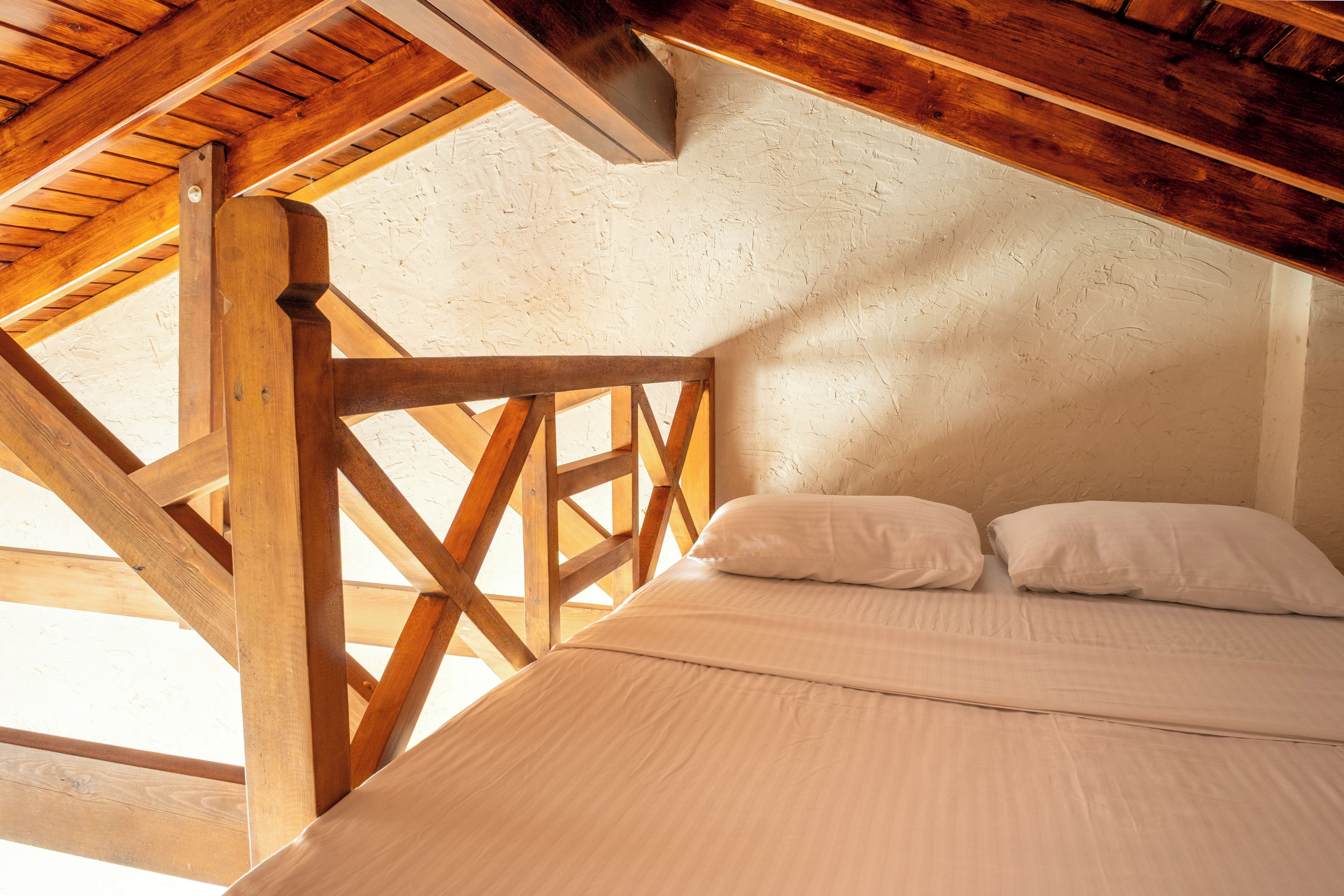 A bedroom with a wooden ceiling structure, a bed with white bedding, and a textured wall.