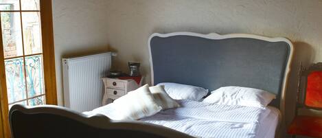 A bedroom with a bed, a radiator, a small table, and a chair.