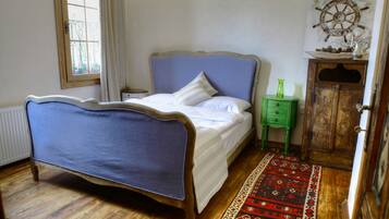 A bedroom with a bed, a wooden cabinet, a green nightstand, a ship's wheel decoration, and a patterned rug.