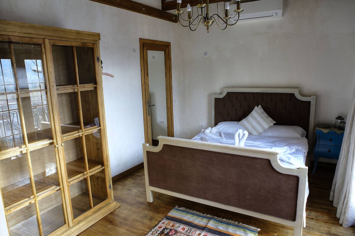 A bedroom with a wooden wardrobe, a bed with a brown headboard, and a blue nightstand.