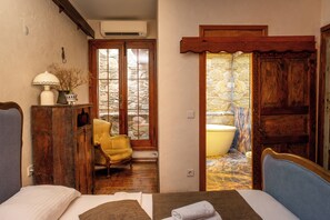Une pièce comprenant un lit, une chaise, une armoire en bois et une salle de bain visible à travers une porte en verre.