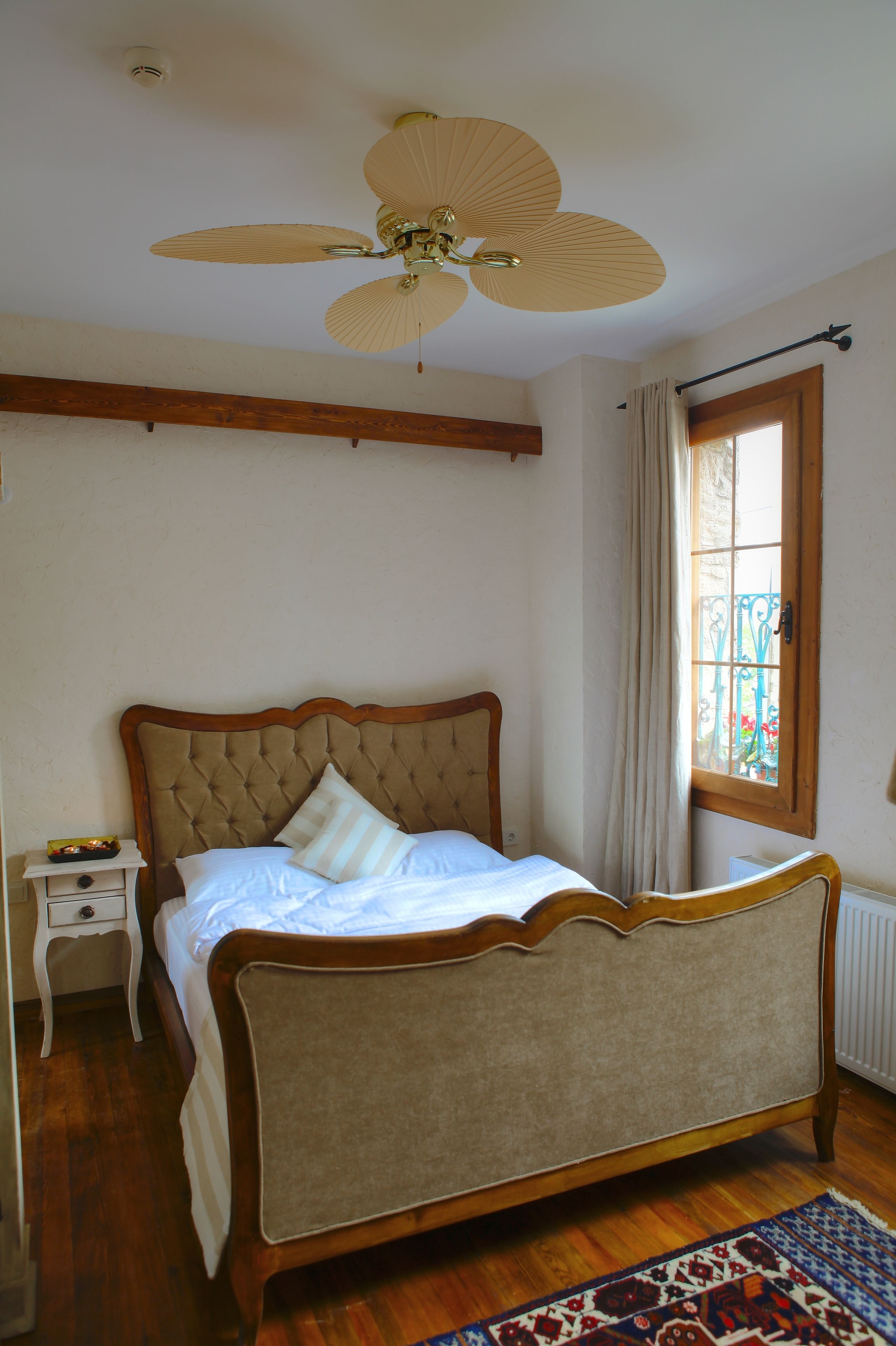 A bedroom with a wooden bed, a ceiling fan, a nightstand, and a window with curtains.