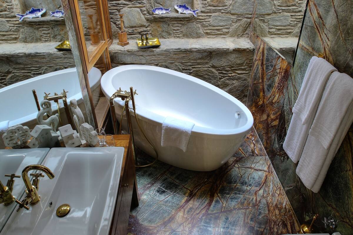 A bathroom with a freestanding bathtub, a sink, and a toilet. The walls are made of stone, and there is a skylight above the bathtub.