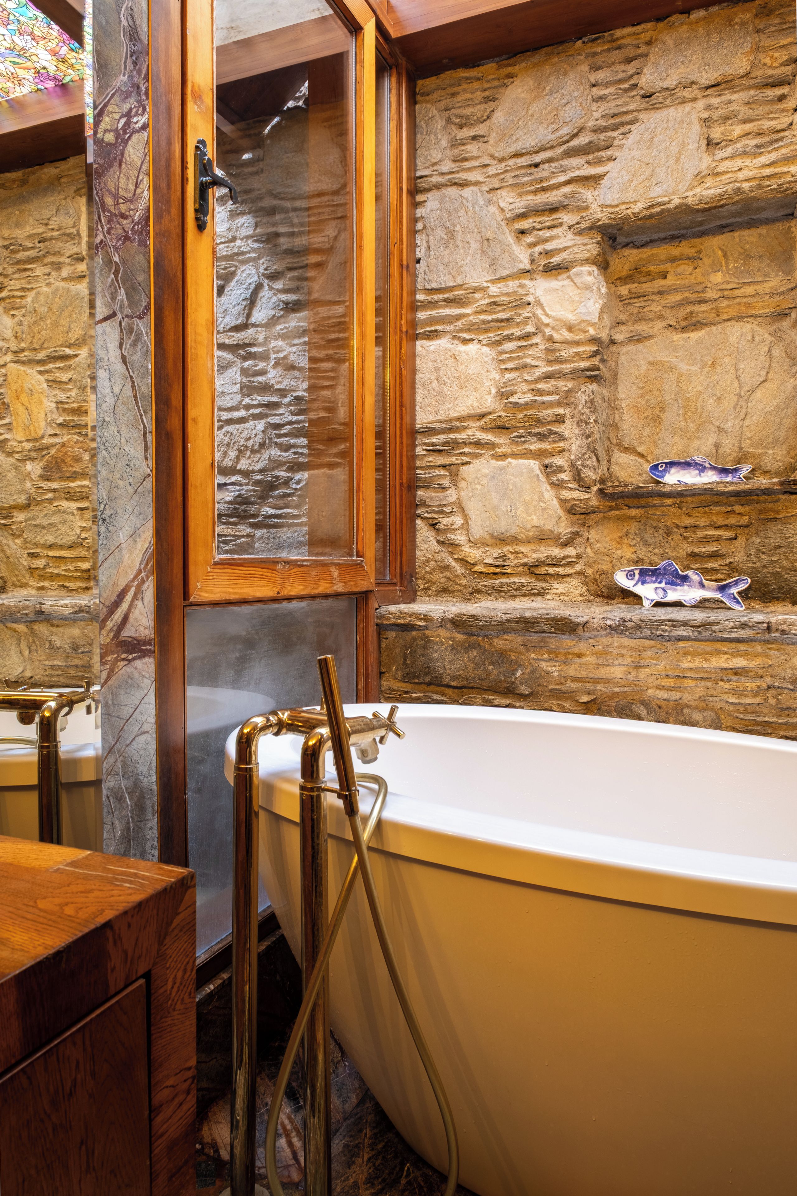 A bathroom with a stone wall, a wooden door, a bathtub, and a wooden cabinet.