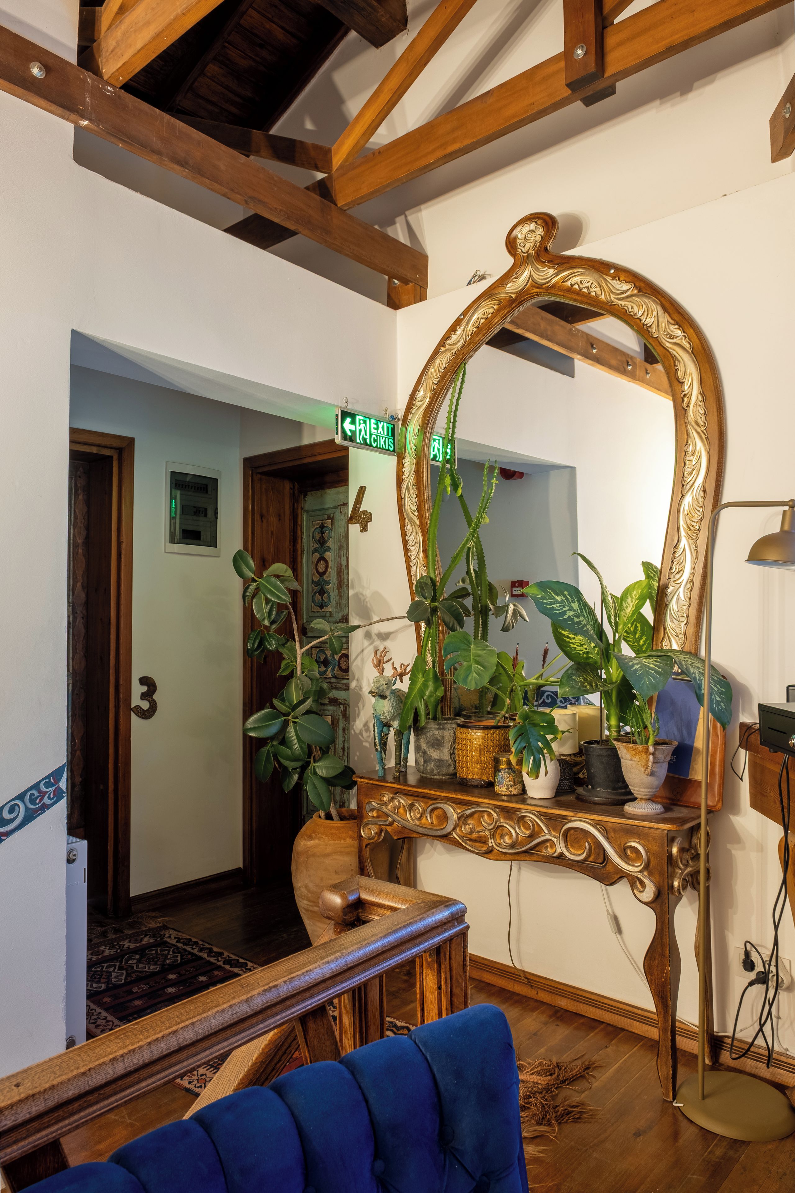 A room with a wooden ceiling, a large ornate mirror, a blue sofa, and various potted plants.