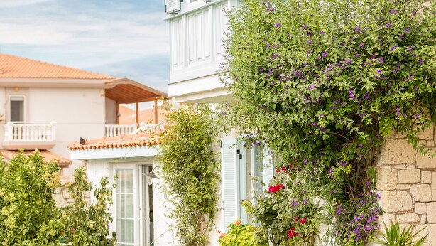 A two-story building with a white facade and a red-tiled roof. There are potted plants and a small garden area in front of the building. - Deniz Kabugu Hotel (Cesme)