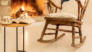 A cozy room with a stone fireplace, a rocking chair, and a table with a book and a cup. - Deniz Kabugu Hotel (Cesme)