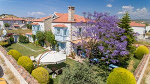 A large house with a stone chimney, a garden with a white umbrella, and a view of the surrounding area. - Deniz Kabugu Hotel (Cesme)