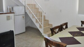 Una cocina con refrigerador, estufa y pileta. Se ve una escalera que sube a otro nivel.