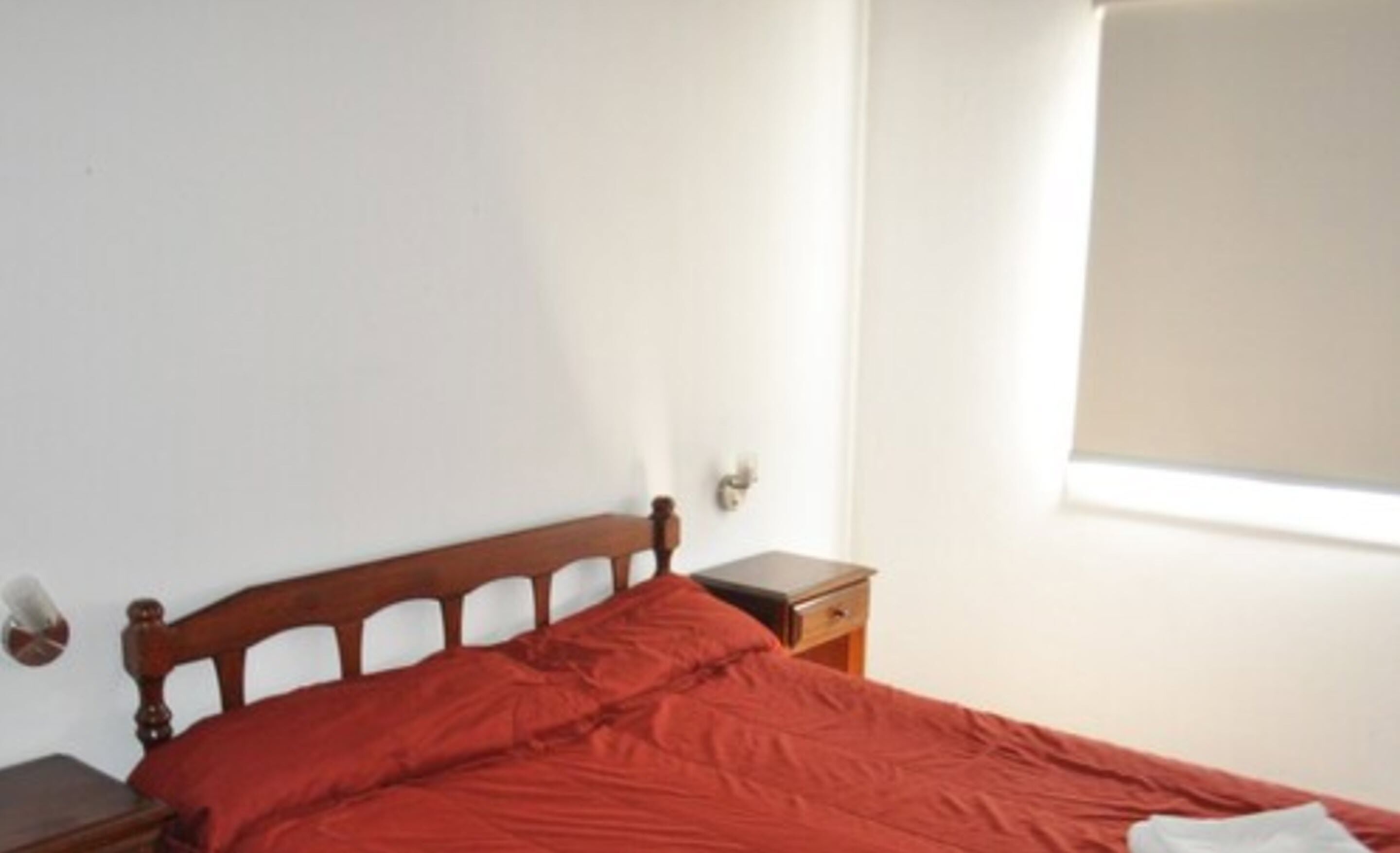 Una cama individual con cabecera de madera en una habitación con paredes blancas y un ventanal.