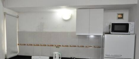 Une cuisine avec des meubles blancs, une cuisinière à gaz, un four à micro-ondes et un réfrigérateur.