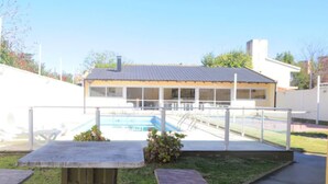 Un edificio con piscina, terraza techada y un pequeño jardín.