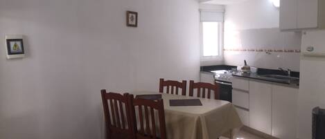 A compact kitchen with a dining table, chairs, and basic appliances.