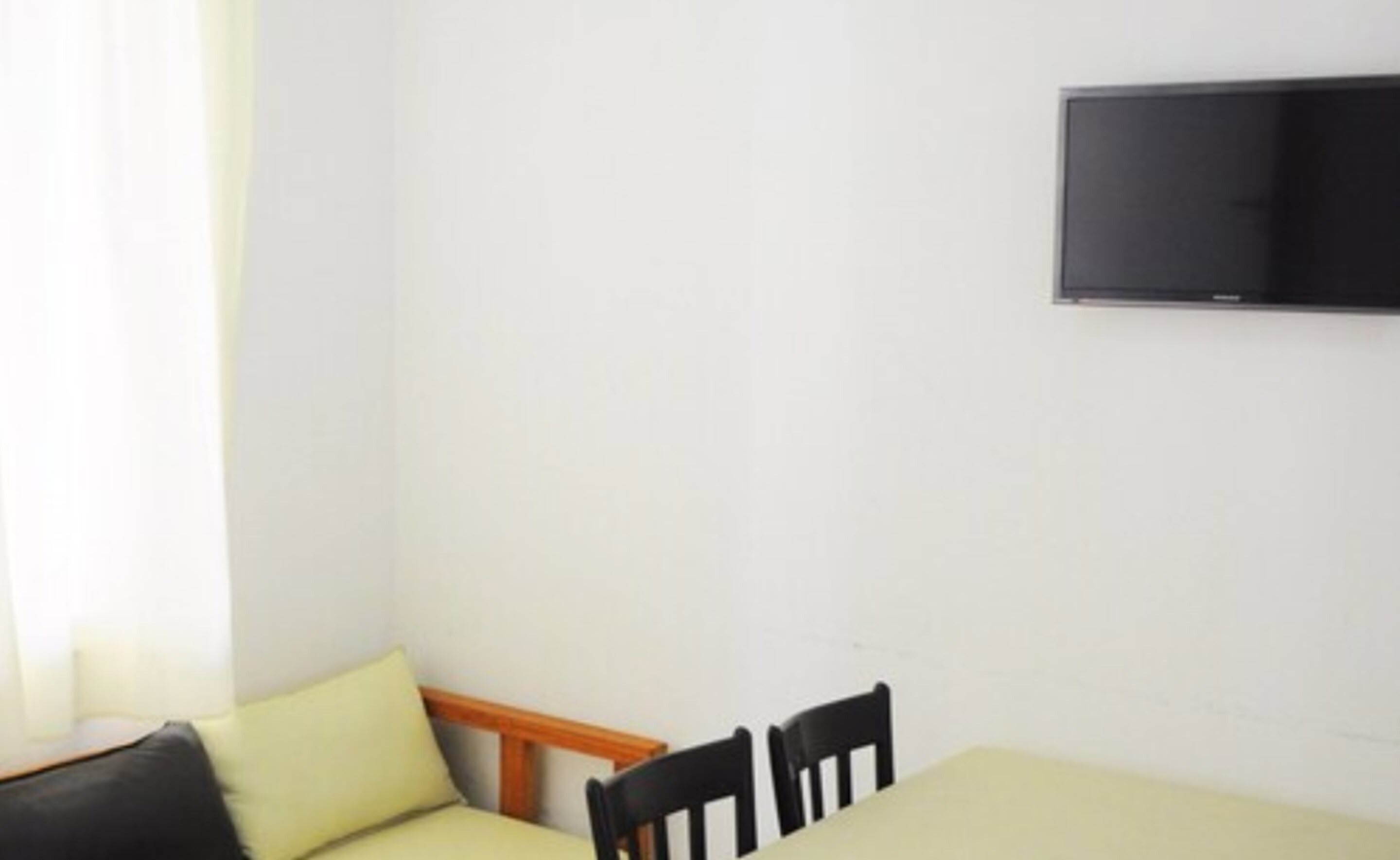 Een kleine kamer met een bed, een stoel en een aan de muur bevestigde televisie.