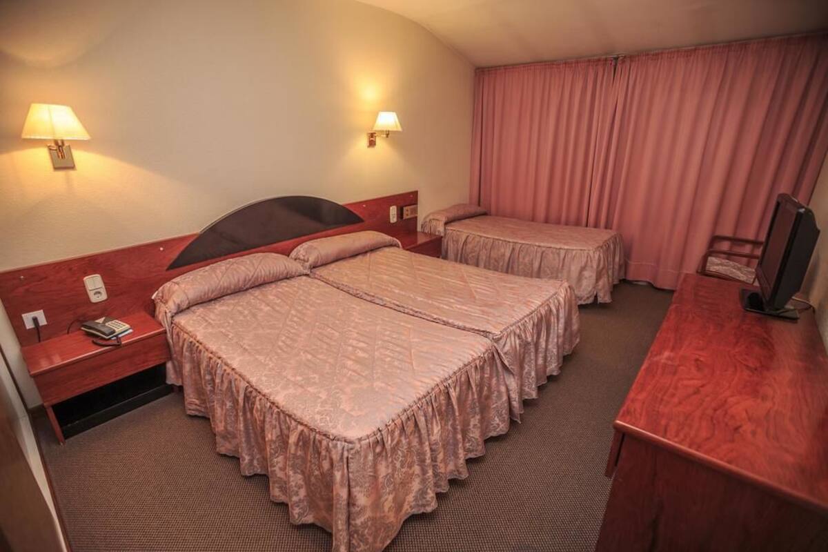 A hotel room with two beds, a desk, a chair, and two bedside lamps.