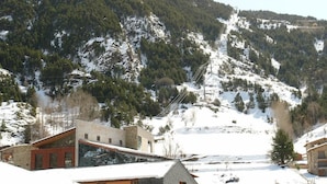 A modern building with a sloped roof, surrounded by snow-covered mountains and trees. - Hotel Roc del Castell (Canillo)