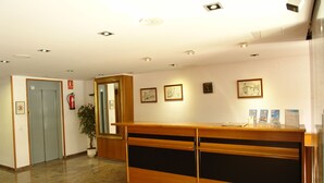 A reception area with a wooden desk, a potted plant, and framed pictures on the wall. - Hotel Roc del Castell (Canillo)