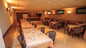 A dining area with multiple tables set for meals, chairs, and a bar area in the background. - Hotel Roc del Castell (Canillo)