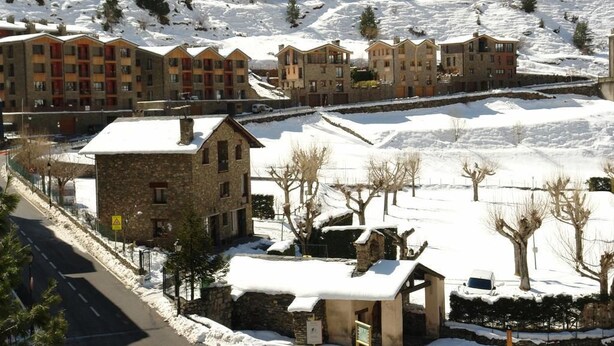 A snow-covered residential area with multi-story buildings, a stone house, and a paved road. - Hotel Roc del Castell (Canillo)