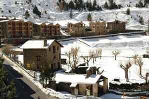 Uma área residencial coberta de neve, com edifícios altos, uma casa de pedra e uma rua pavimentada.