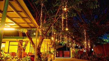 An outdoor area with a covered seating area, potted plants, and a pathway leading to a gated entrance.
