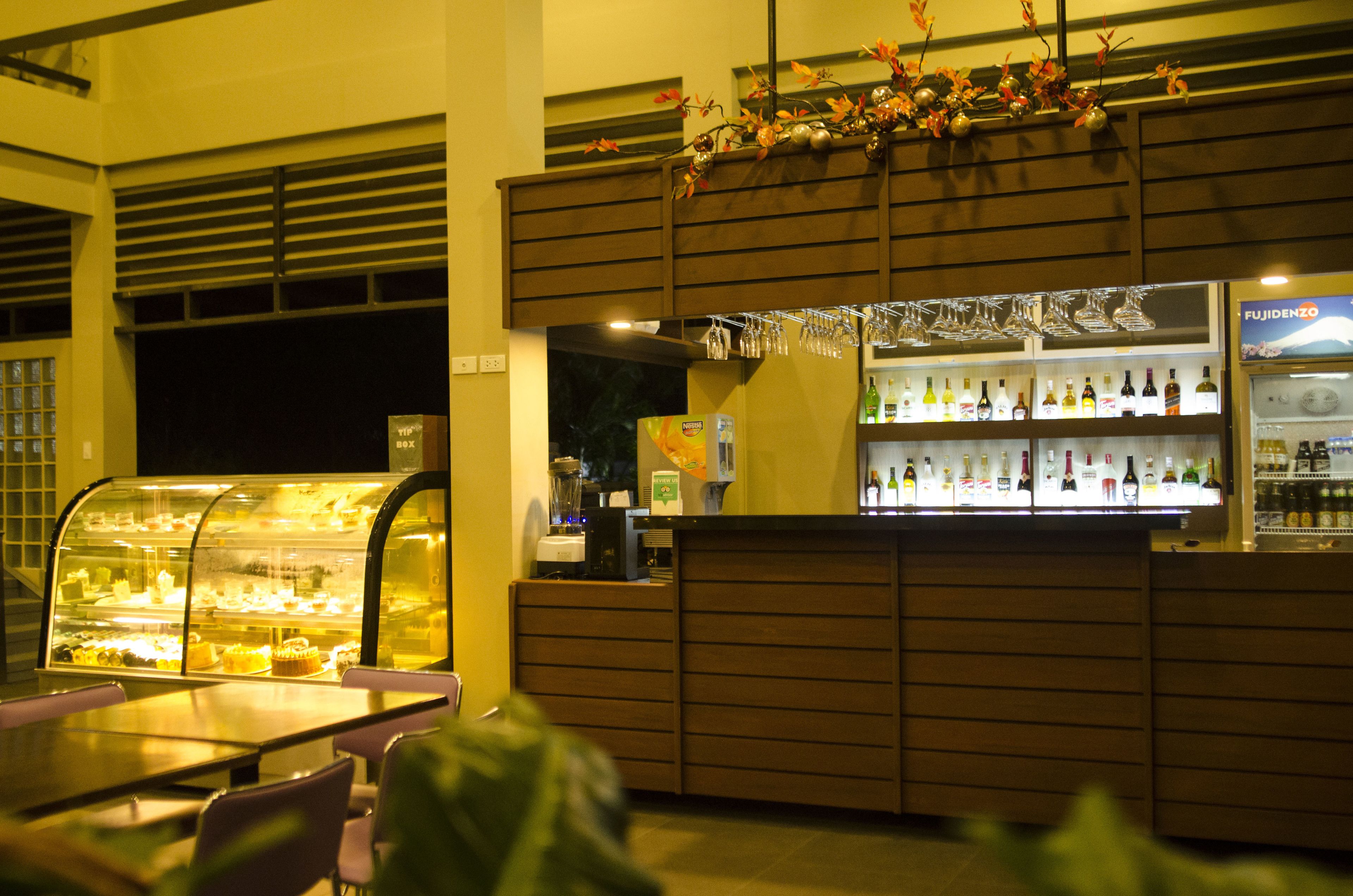 Un restaurante con una vitrina de postres, una zona de bar con botellas y un área de mesas.