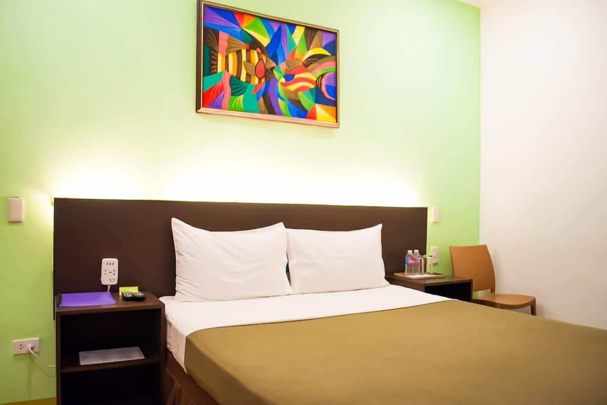 Ein Hotelzimmer mit Bett, Nachttisch, Lampe, einem Bild an der Wand und einem Sessel.