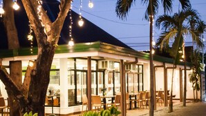 Un restaurante con terraza, palmeras y luces colgantes.