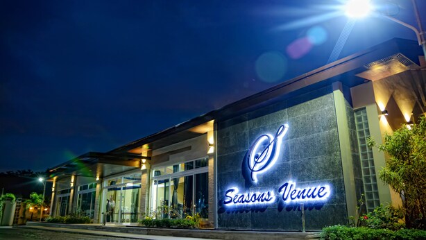 Exterior de un hotel por la noche con un letrero iluminado que dice "Seasons Venue".