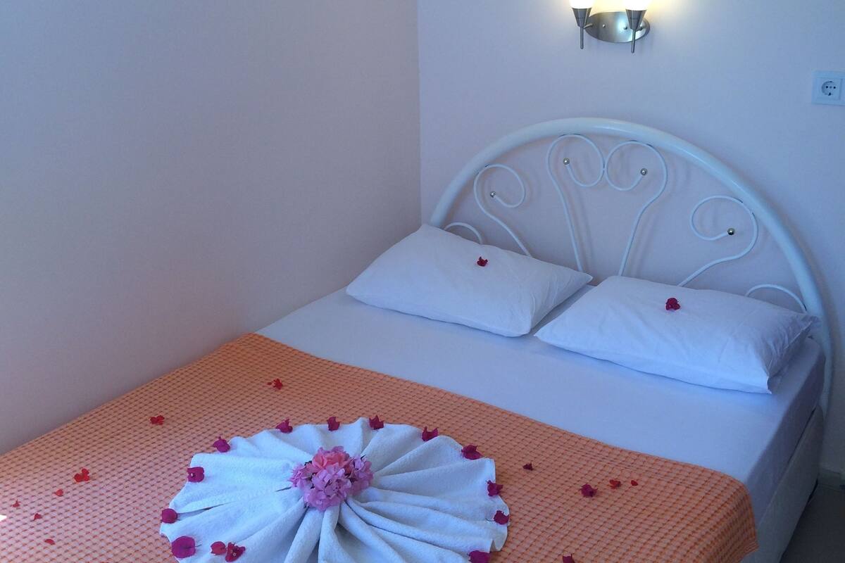 A neatly made bed with a white headboard, a decorative towel centerpiece, and a warm orange blanket.