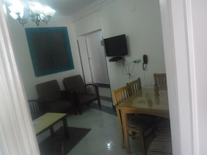 A living room with a sofa, a dining table, and a TV mounted on the wall. - Jewel Mandara Apartments (Alexandria)