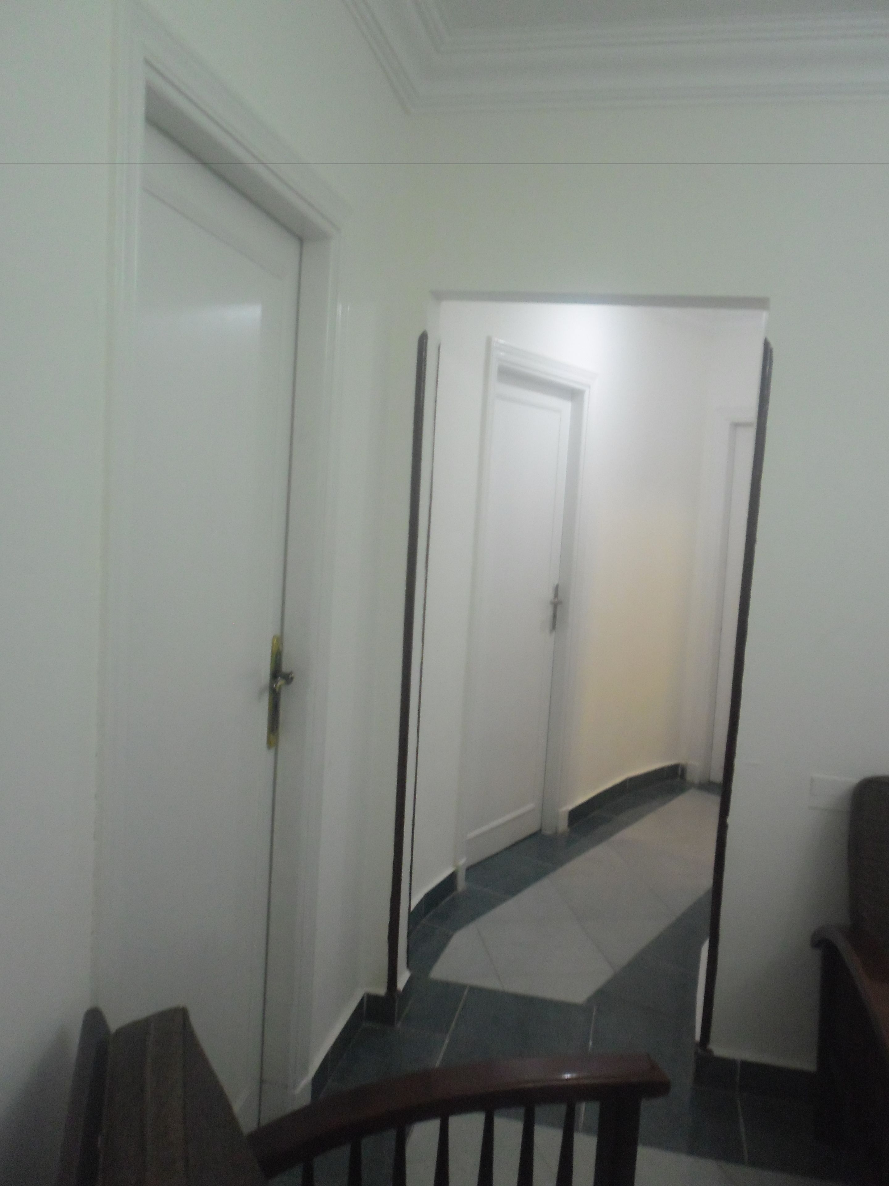 A hallway with a wooden handrail, white doors, and a tiled floor.
