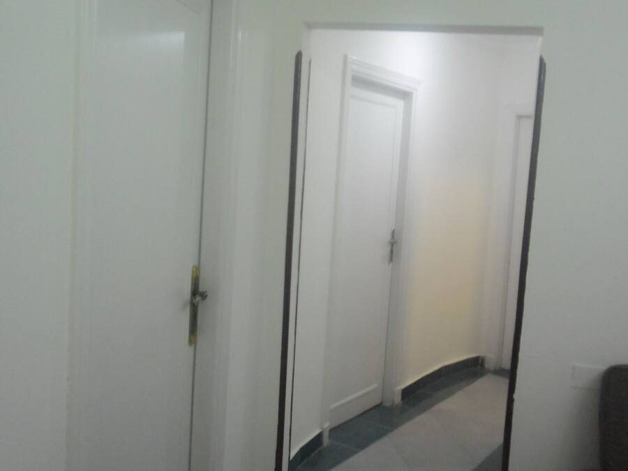 A hallway with a wooden handrail, white doors, and a tiled floor.