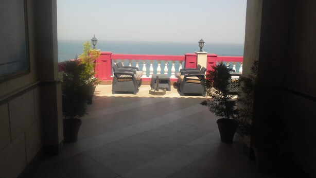 A balcony with outdoor seating and potted plants, overlooking a body of water. - Jewel Mandara Apartments (Alexandria)