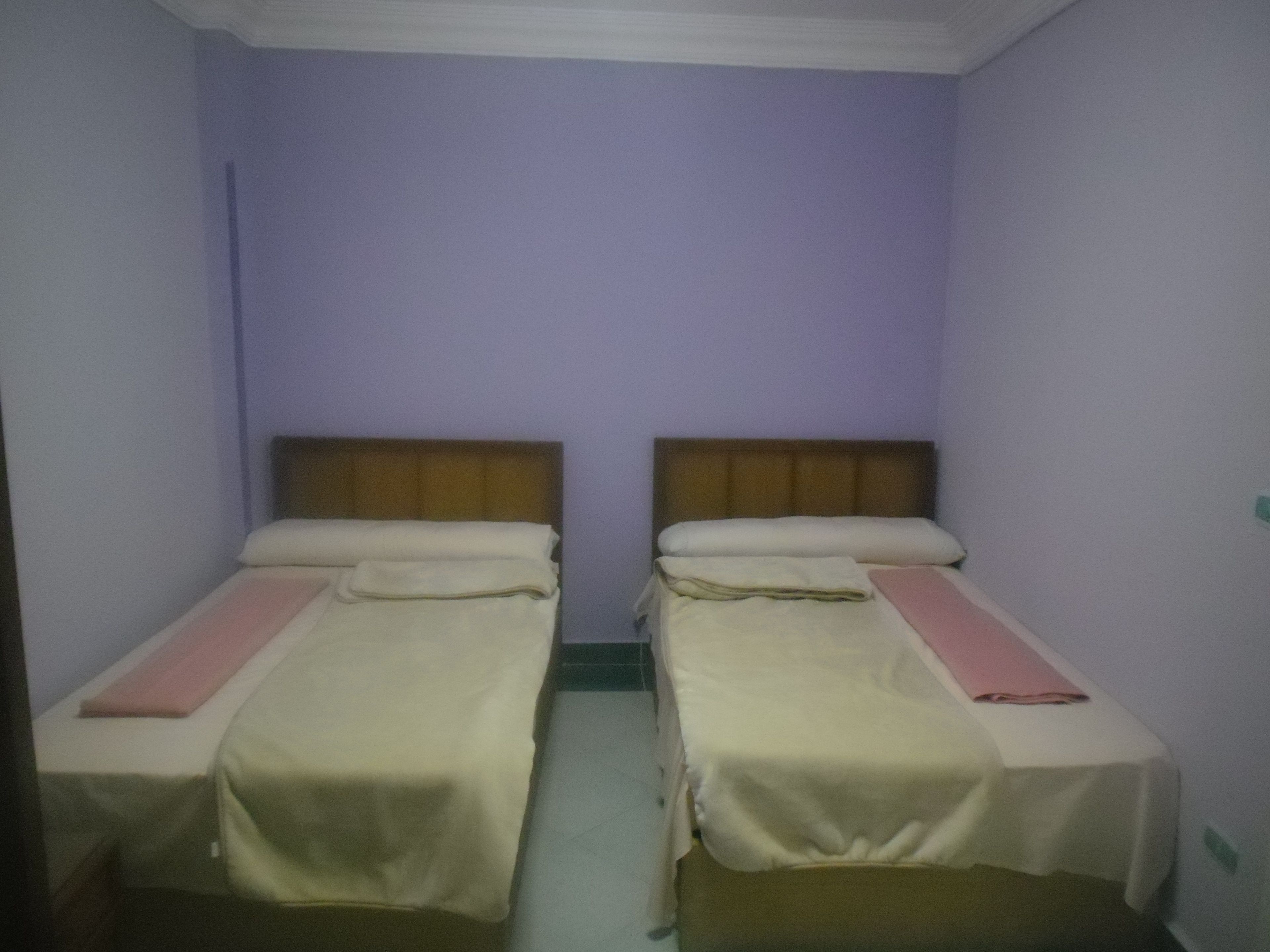 Une chambre double avec deux lits simples, chacun doté d’une tête de lit en bois et de linge de lit blanc.