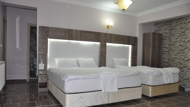 A bedroom with a large bed, a nightstand, and a stone wall. - Mevlana Palace (Konya)