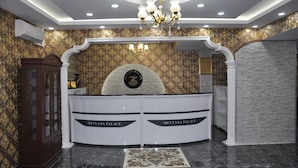 A reception area with a chandelier, a reception desk, and a wall with a patterned wallpaper. - Mevlana Palace (Konya)