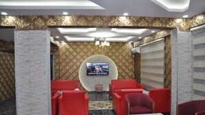 A lobby with red seating, a TV screen, patterned wallpaper, and a chandelier. - Mevlana Palace (Konya)