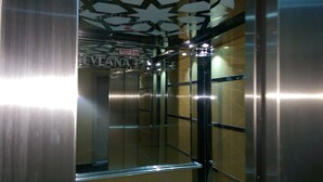 An elevator interior with metallic walls, a reflective ceiling, and a sign indicating a 10-minute wait. - Mevlana Palace (Konya)