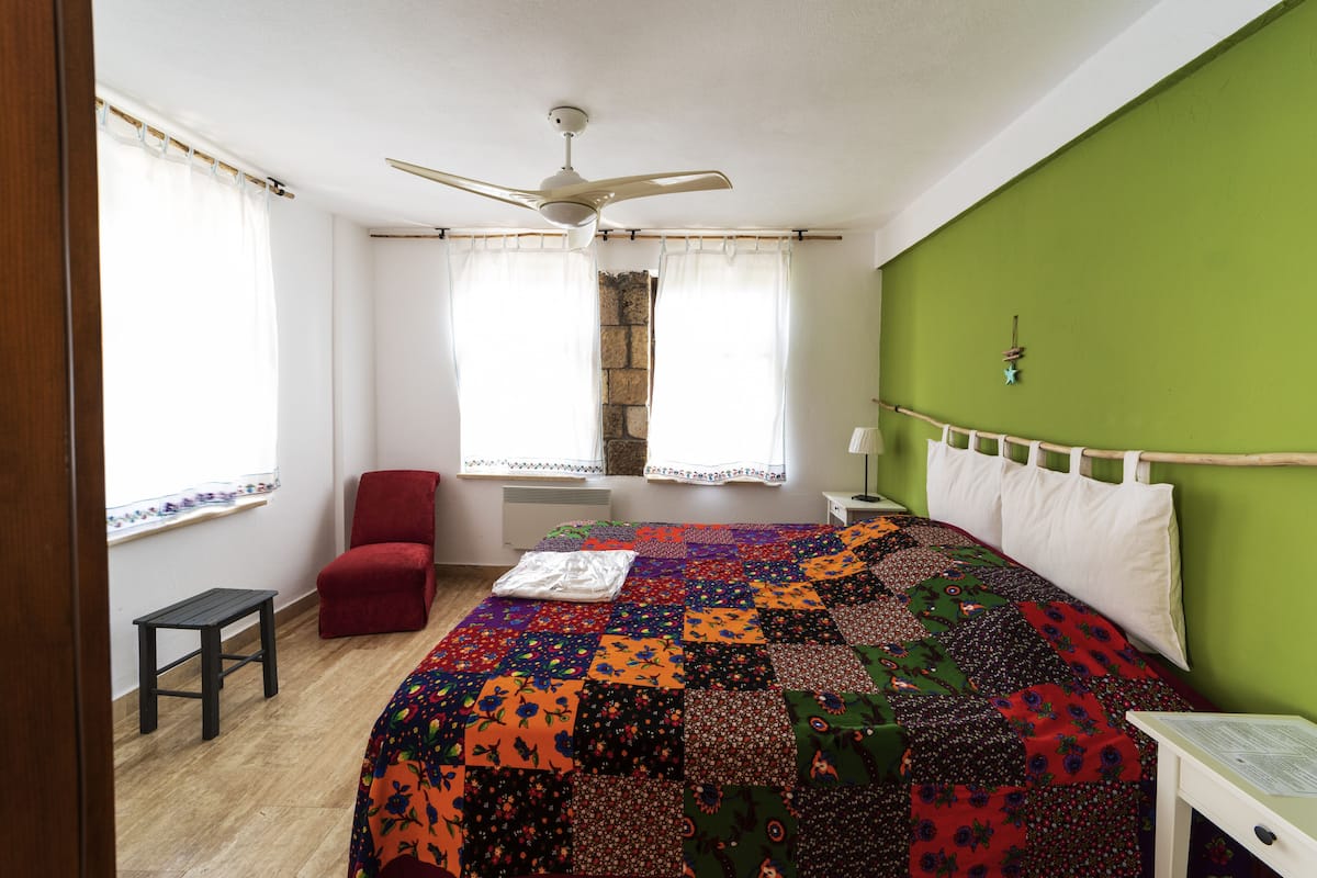 A bedroom with a large bed, a red chair, a small table, and a ceiling fan.