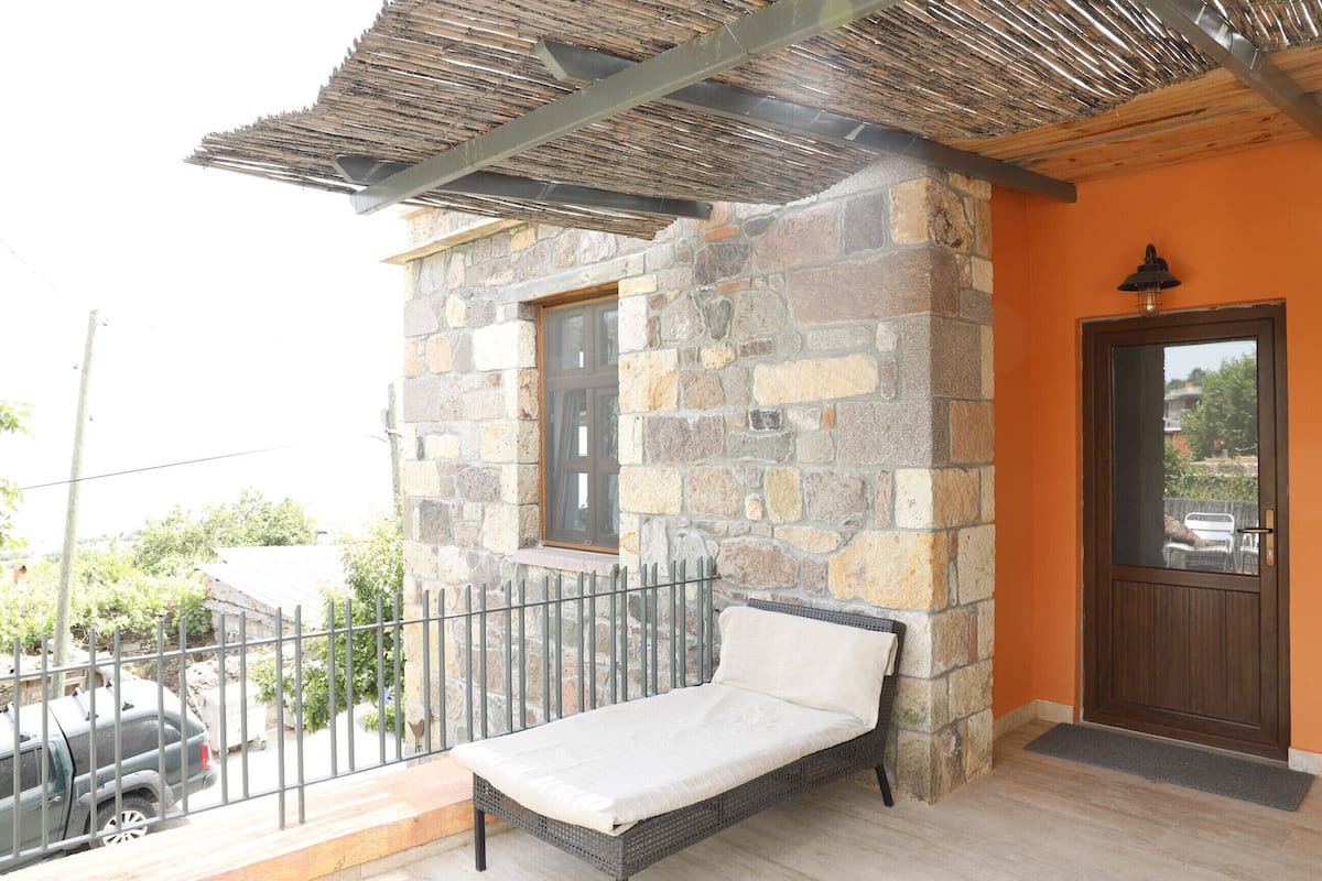 A balcony with a wicker sofa, a stone wall, and a wooden door.