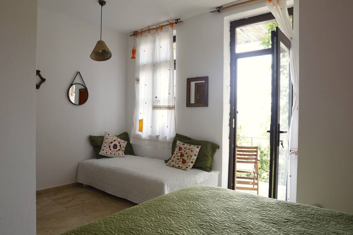 A bedroom with two beds, a hanging light, a window with curtains, and a door leading outside.