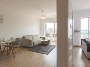 Un salon moderne avec un canapé, une table à manger et des chaises, un balcon offrant une vue dégagée et un panorama sur la ville visible à travers la fenêtre.