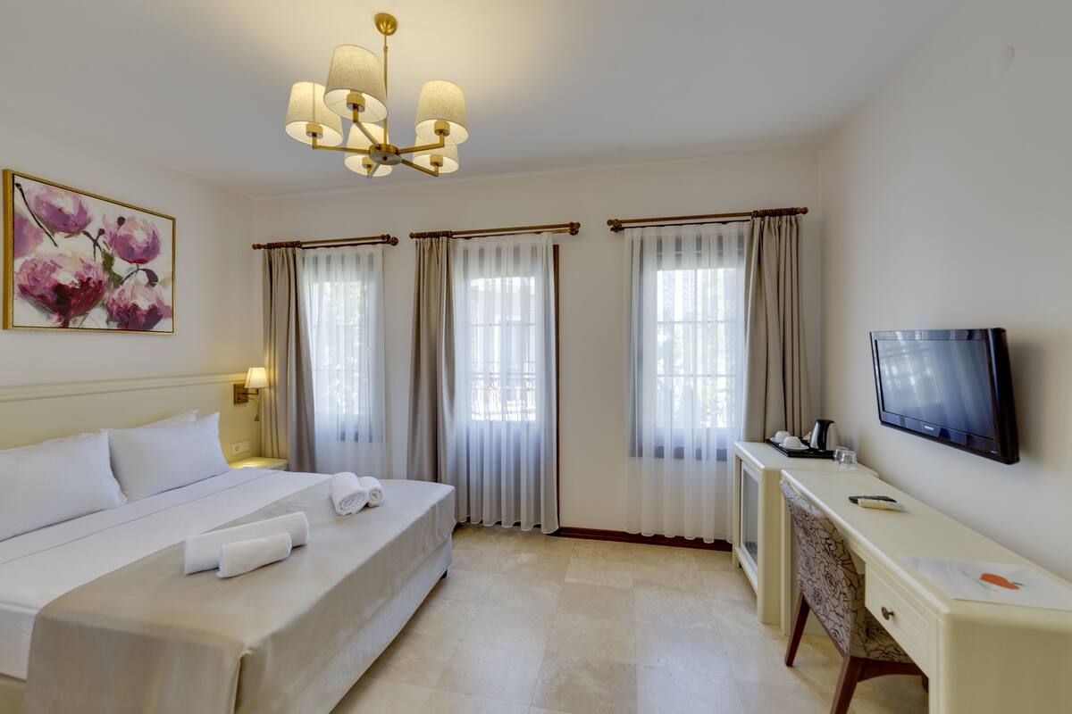 A hotel room with a bed, a desk, a television, and a painting on the wall.