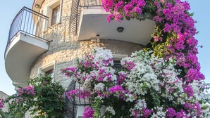 A building with a stone facade, a balcony with metal railings, and lush flowering plants. - Orcey Hotel (Datça)