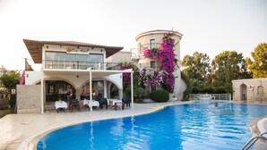 A swimming pool with a restaurant patio, a stone building with a balcony, and a round tower with pink flowers. - Orcey Hotel (Datça)